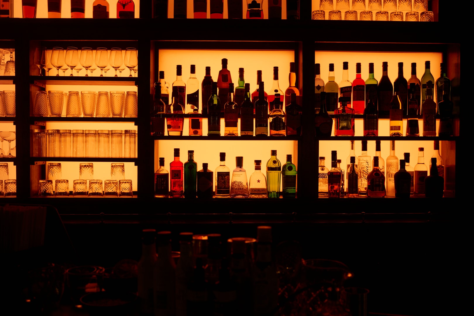 Illuminated bar with wine bottles backlit by warm golden lighting